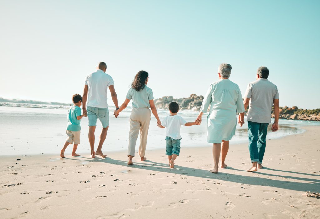 Big family, holding hands and walking outdoor on beach with children, grandparents and parents . Men, women and boy kids walk by sea for summer travel vacation or holiday with love, care and support.